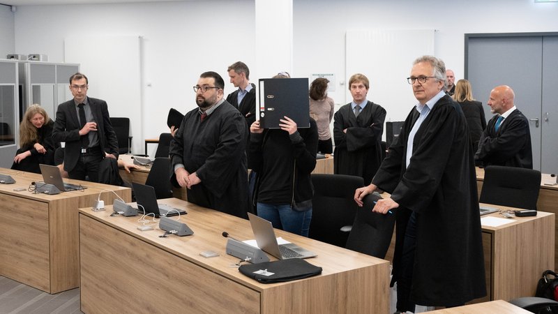 Die Angeklagte Lina E. (r) steht bei der Fortsetzung des Prozesses im Oberlandesgericht (OLG) Dresden im Verhandlungssaal und hält einen Aktenordner vor ihr Gesicht. 