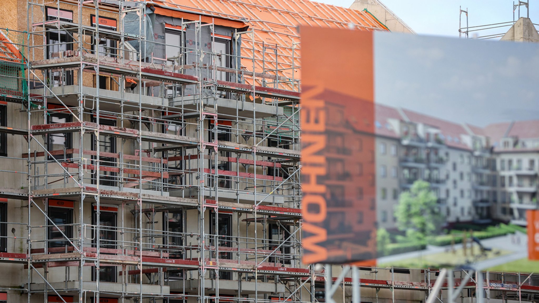 Eine Bautafel steht vor der Baustelle mehrerer Miethäuser.