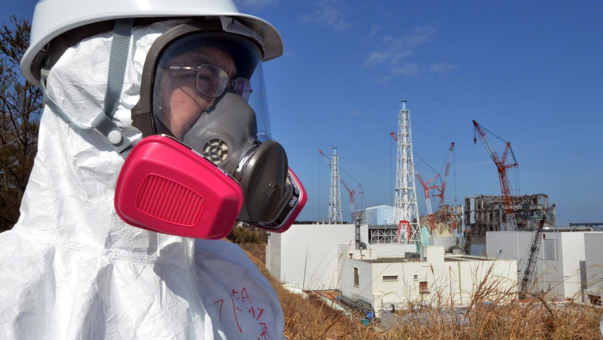 Besucher mit Atemmaske vor dem Atomkraftwerk Fukushima