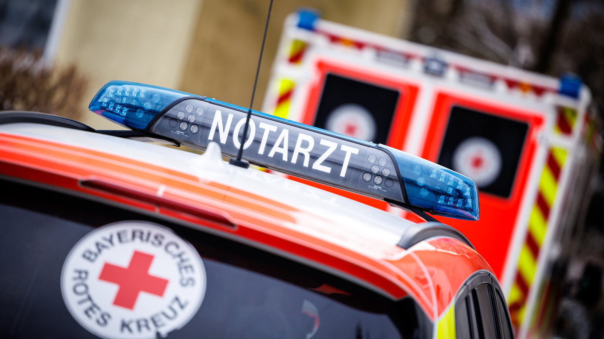 Ein Notarzteinsatzfahrzeug steht während eines Rettungseinsatzes an einem Einsatzort geparkt hinter einem Rettungswagen vom Bayerischen Roten Kreuz. (Symbolbild)
