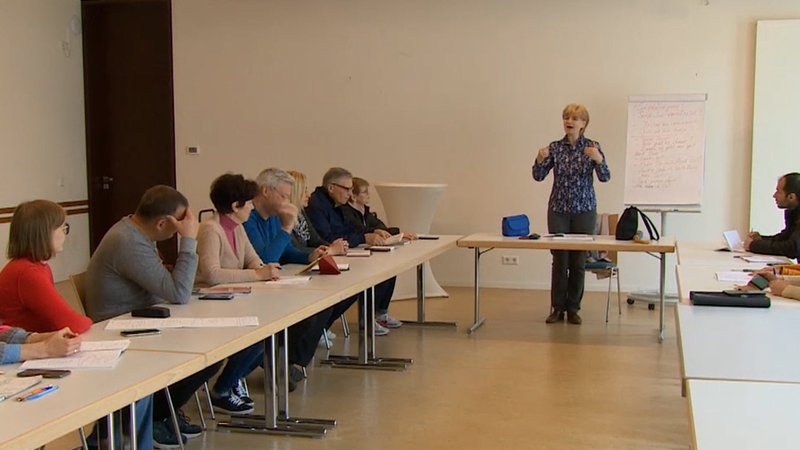 Menschen an Tischen in U-Form im Deutschunterricht.