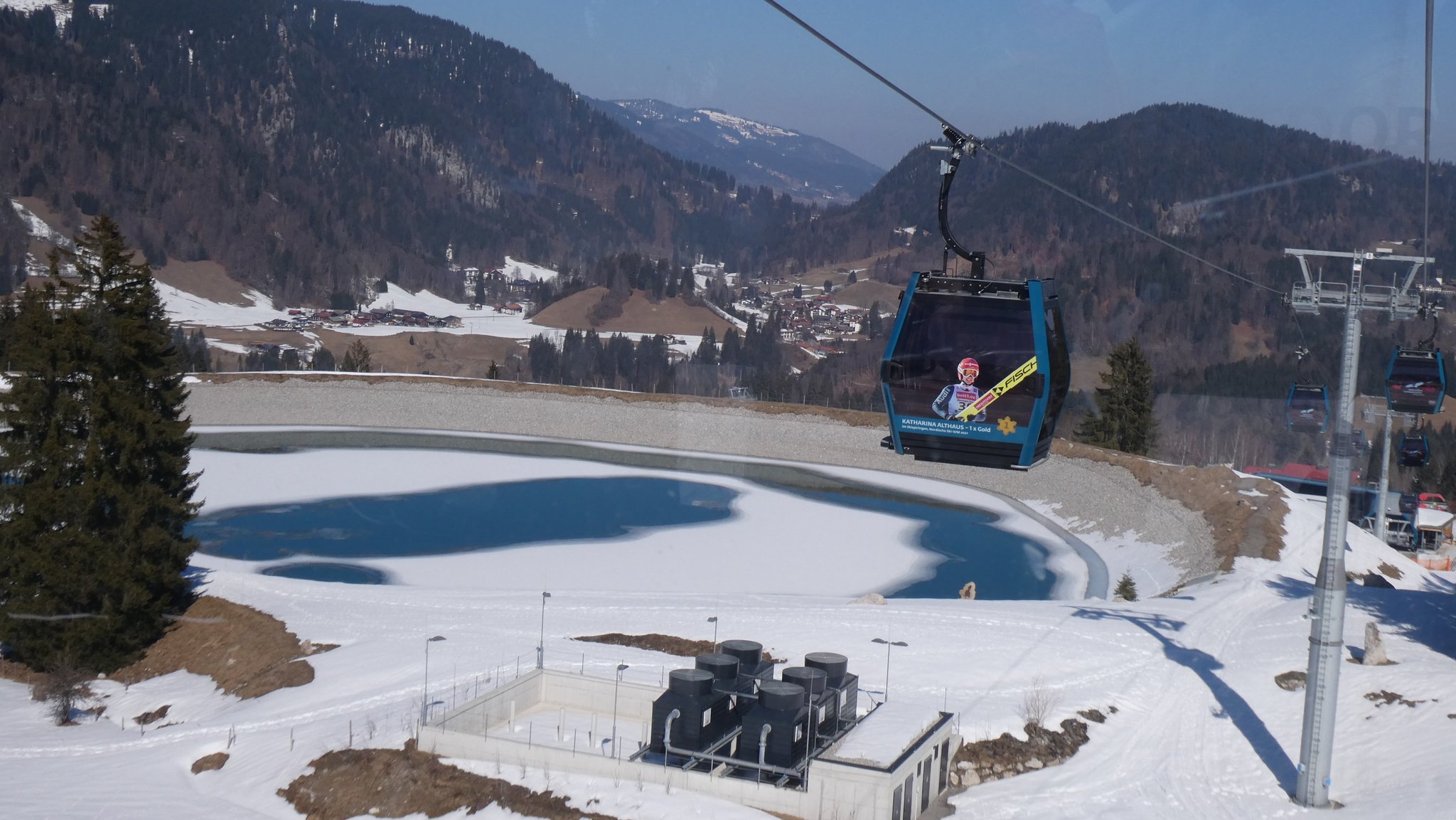 Blick von der Skipiste aus auf ein Kunstschnee-Speicherbecken sowie einen Ort im Tal.