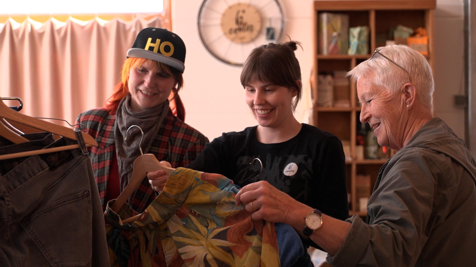 Drei Frauen sehen sich Kleidungsstücke an.