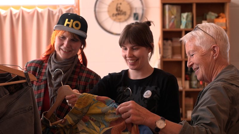 Drei Frauen sehen sich Kleidungsstücke an. | Bild: Bayerischer Rundfunk 2025 Drei Frauen sehen sich Kleidungsstücke an.