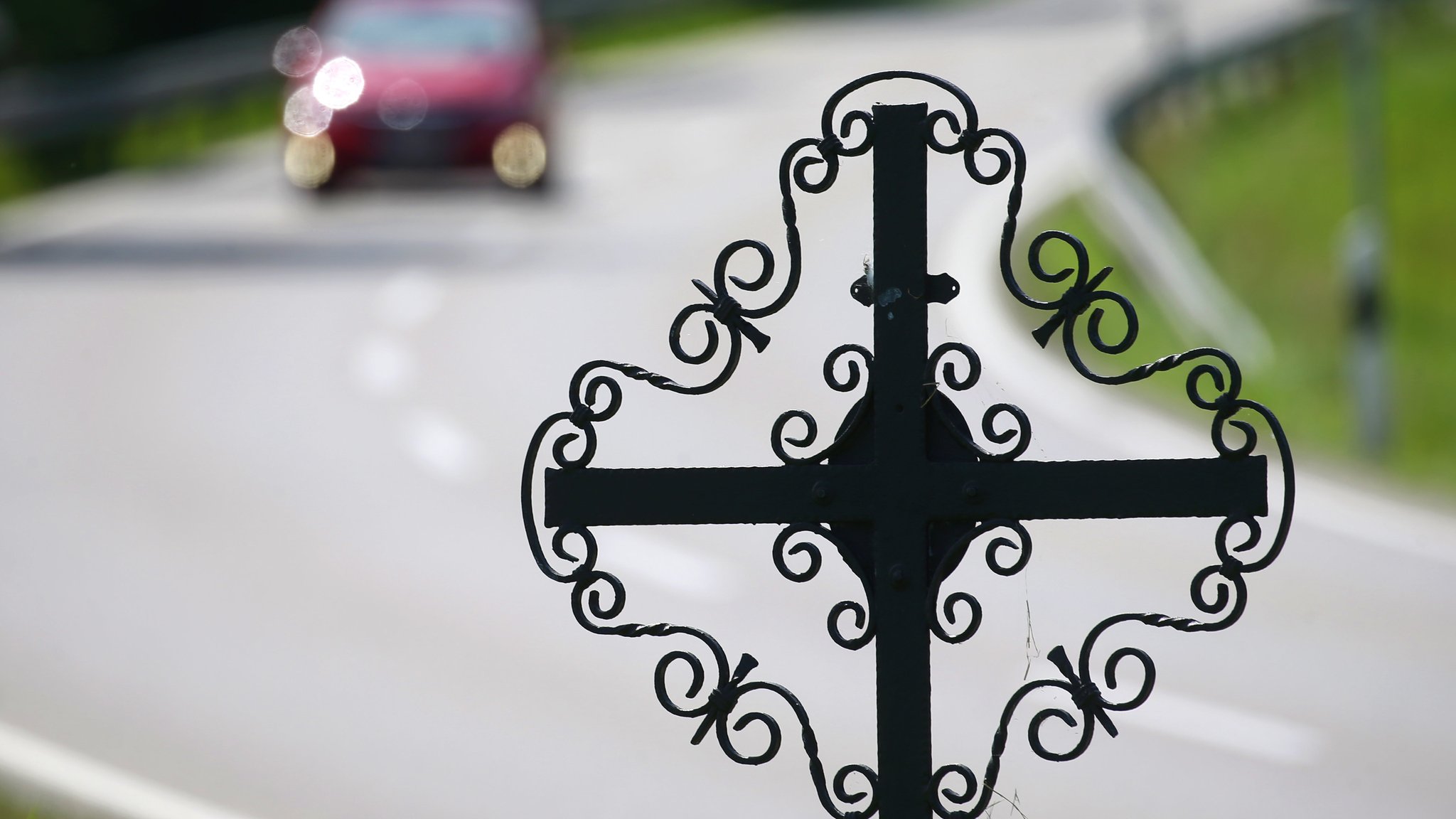 Ein Auto fährt hinter einer mit einem Kreuz markierten Unfallstelle. 