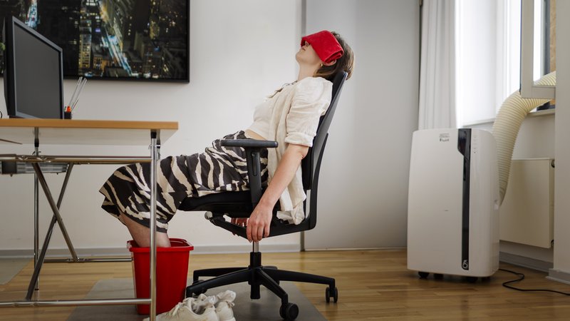 Frau sitzt am Schreibtisch mit Füßen im Wassereimer, Kühltuch und Klimagerät | Bild: picture alliance / Ute Grabowsky/photothek.de | Ute Grabowsky Frau sitzt am Schreibtisch mit Füßen im Wassereimer, Kühltuch und Klimagerät