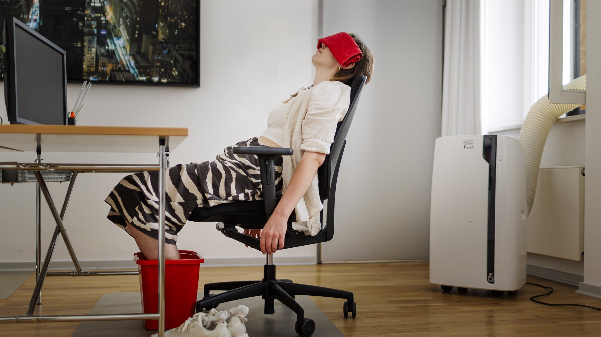 Frau sitzt am Schreibtisch mit Füßen im Wassereimer, Kühltuch und Klimagerät | Bild: picture alliance / Ute Grabowsky/photothek.de | Ute Grabowsky Frau sitzt am Schreibtisch mit Füßen im Wassereimer, Kühltuch und Klimagerät