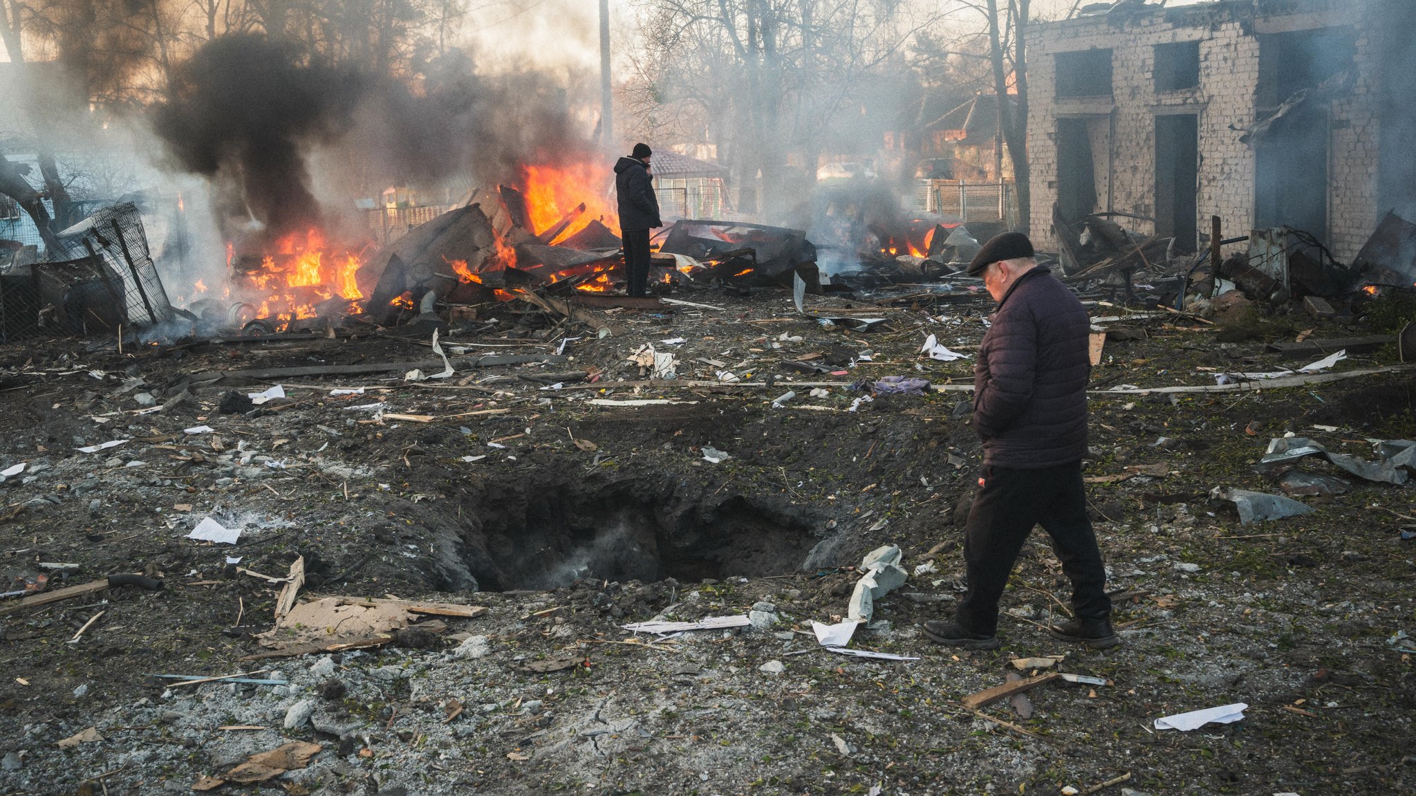 Charkiw, Ukraine, 07.03.25: Zwei Menschen stehen nach einem russischen Raketeneinschlag vor brennenden Trümmern.