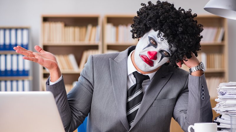 Mann im Anzug und Clownsmaske am Schreibtisch mit Laptop | Bild: colourbox.com Mann im Anzug und Clownsmaske am Schreibtisch mit Laptop
