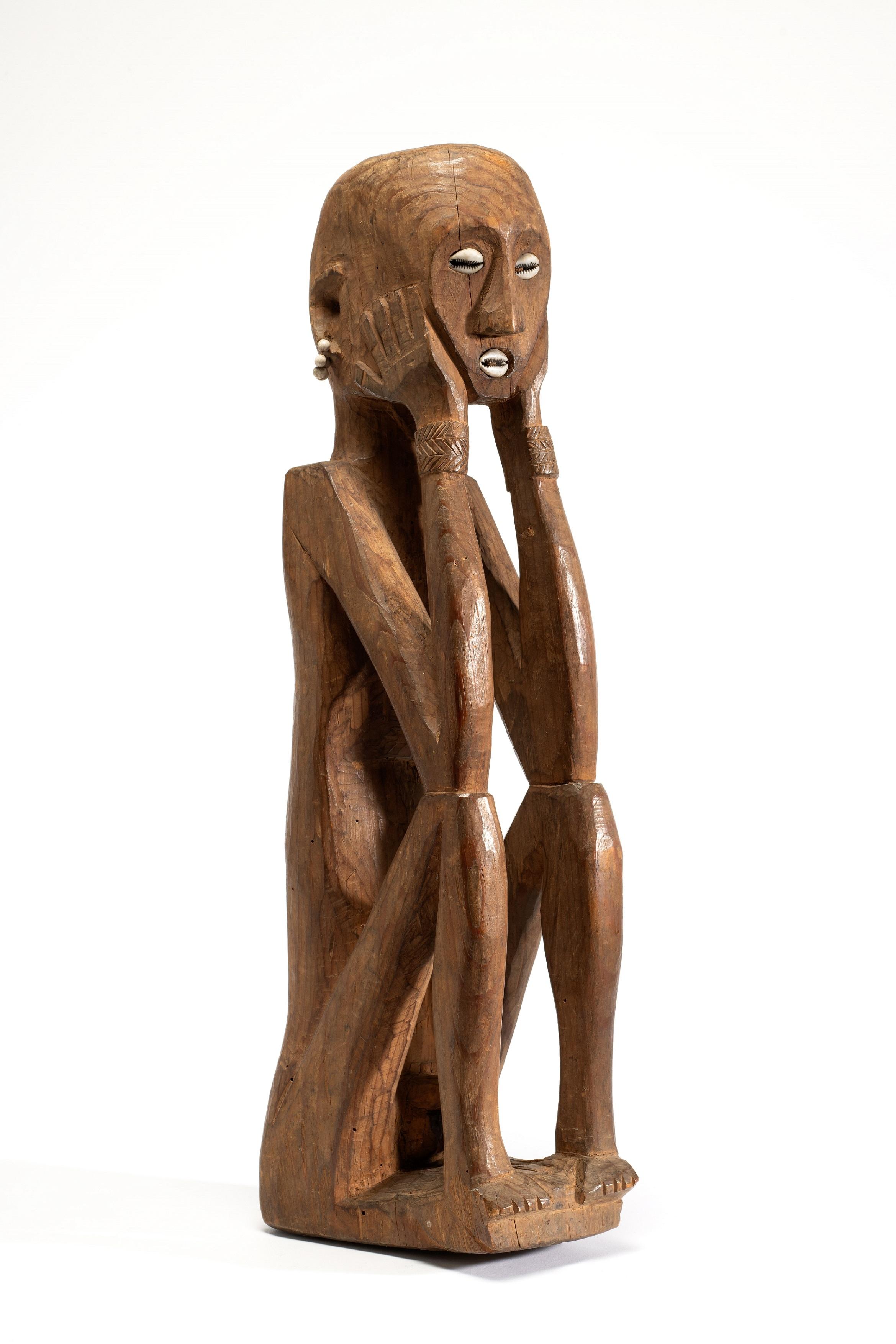 Eine geschnitzte Menschfigur aus blankem Holz mit eingelegten Muscheln als Augen und Mund