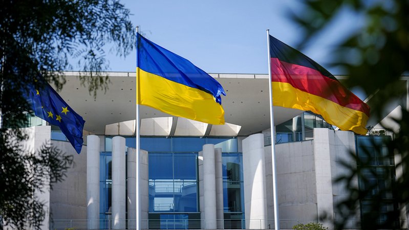 Die Fahne der Ukraine weht zwischen einer EU- und einer deutschen Fahne vor dem Bundeskanzleramt