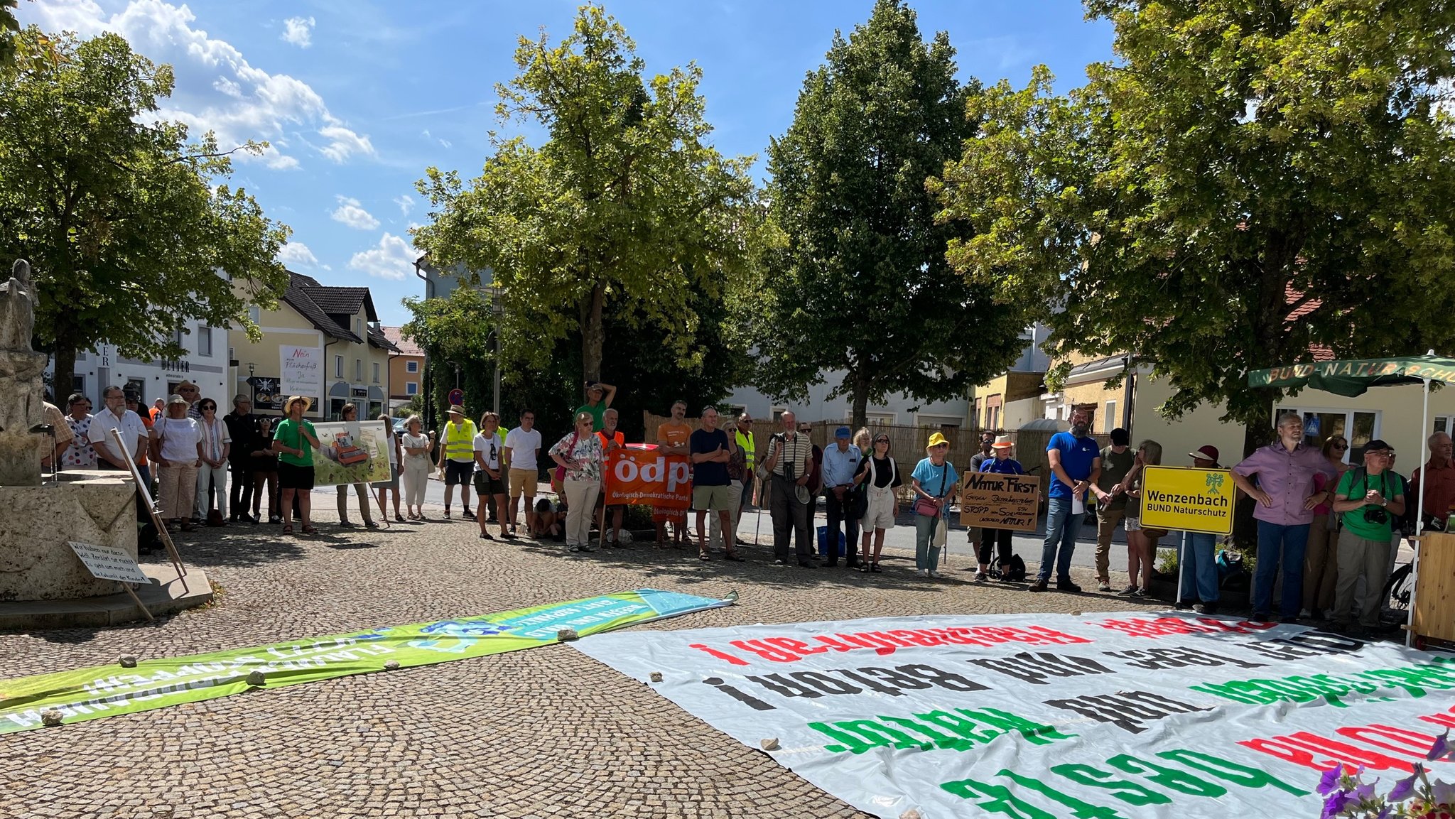 Mehrere Teilnehmer der Demo halten Schilder und Fahnen hoch, am Boden liegen beschriftete Transparente 