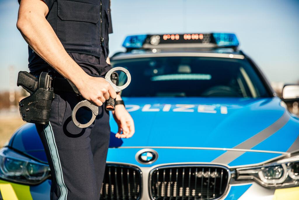 Ein Polizist steht vor einem Streifenwagen und hält ein Paar Handschellen in der Hand.