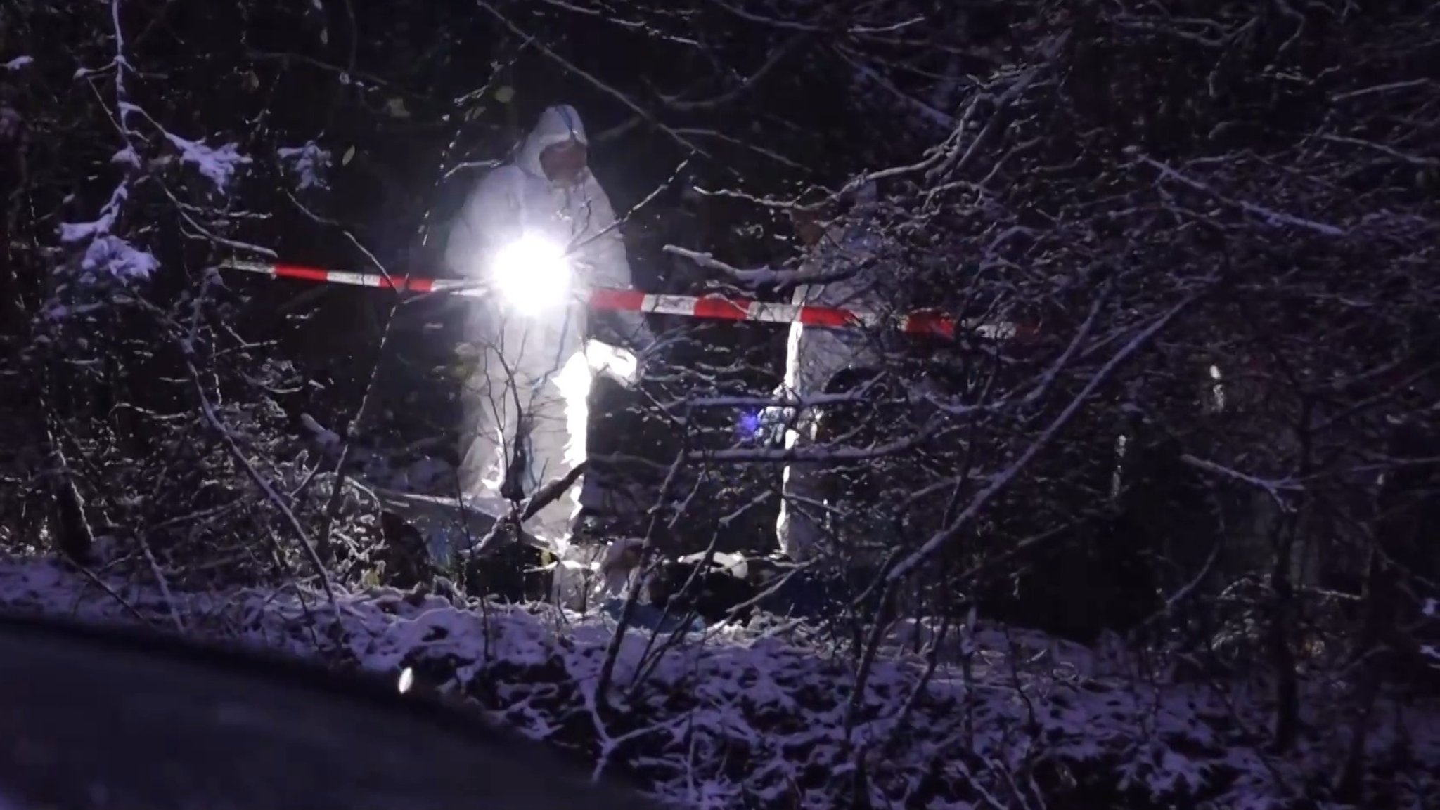 Polizisten in weißen Overalls suchen den schneebedeckten Boden ab. 