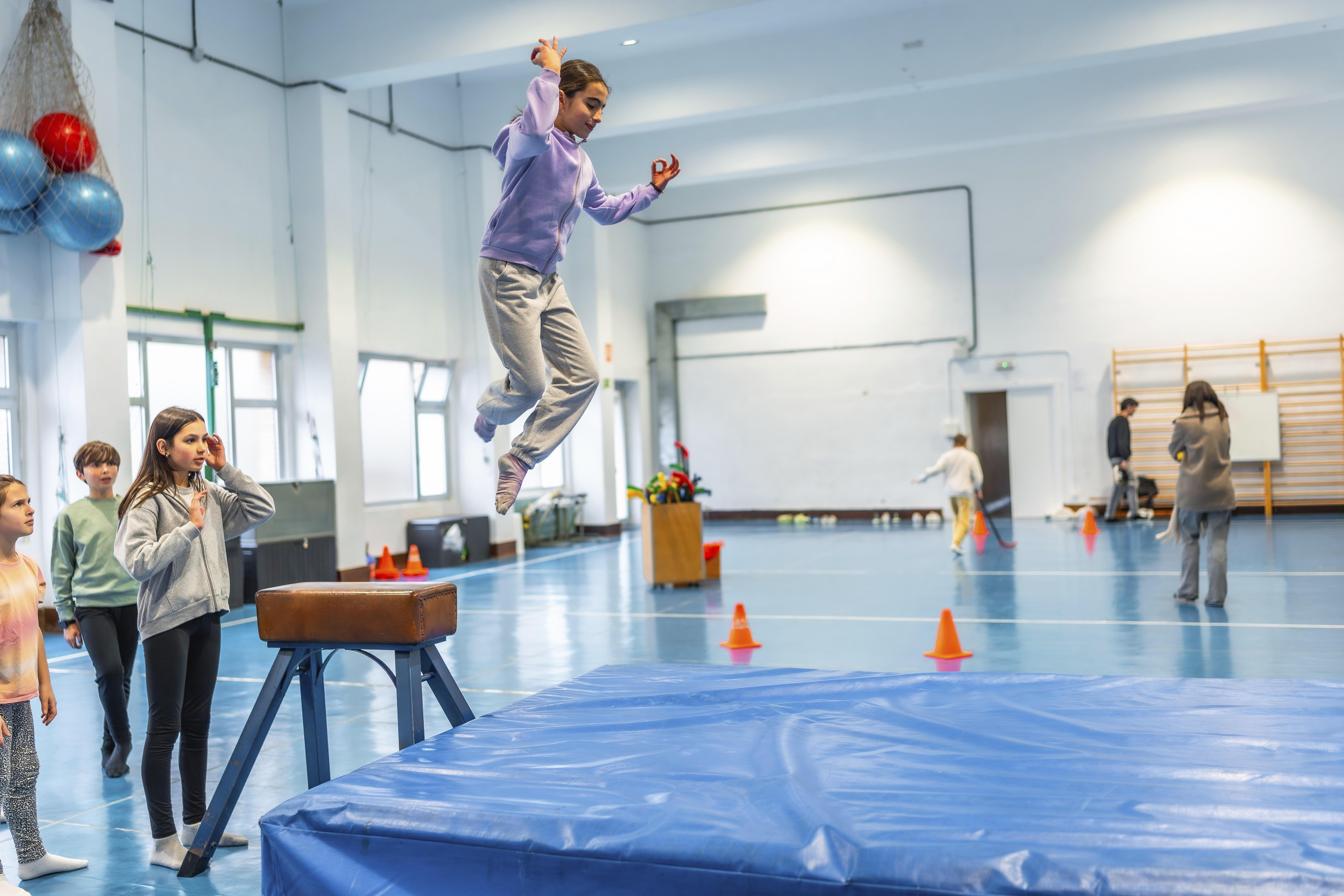 ARCHIV (09.02.2025): Schülerin beim Voltigieren im Sportunterricht, beobachtet von ihren Mitschülern und ihrer Lehrerin, demonstriert Sportlichkeit und Geschicklichkeit
