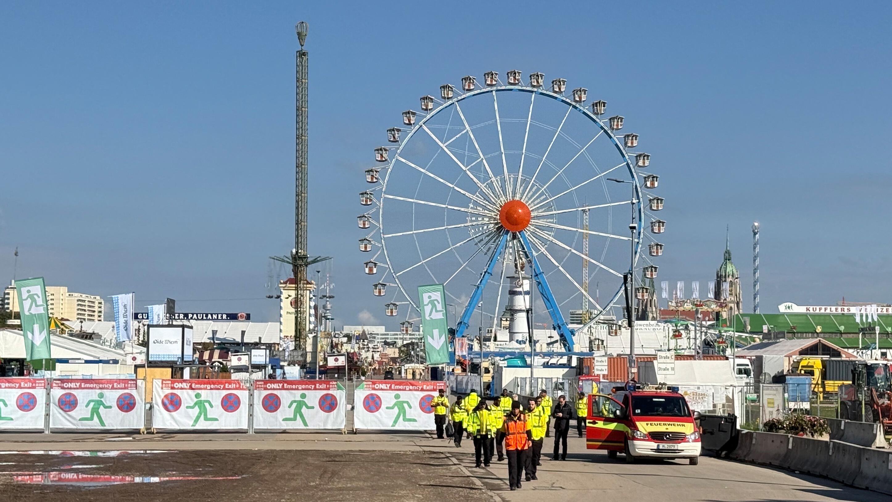 Sicherheitskräfte und Einsatzkräfte der Feuerwehr stehen vor dem Gelände vom Oktoberfest.