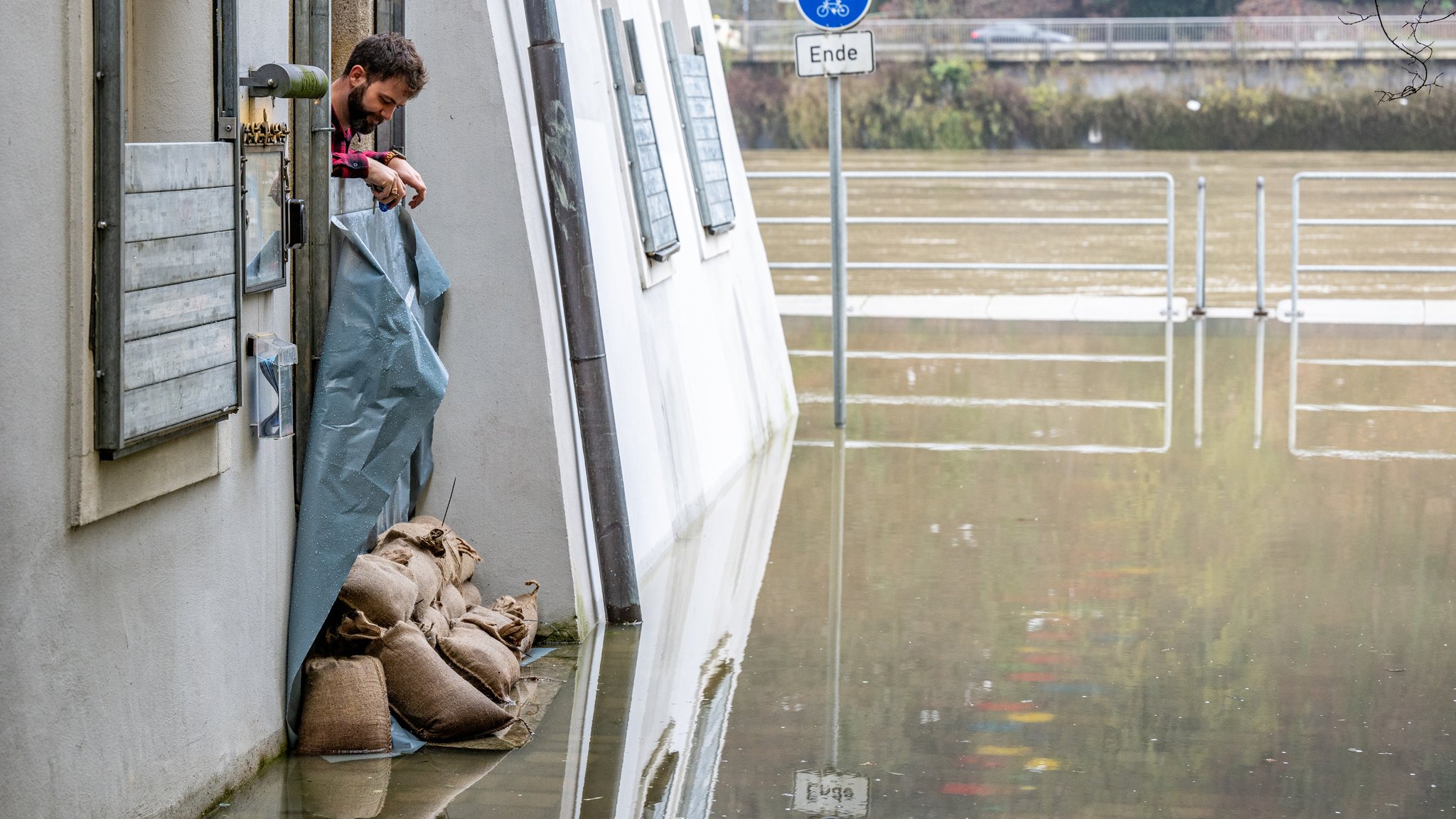 Ein Mann schaut aus einem mit Sandsäcken geschützten Haus auf das Hochwasser der Donau in Passau