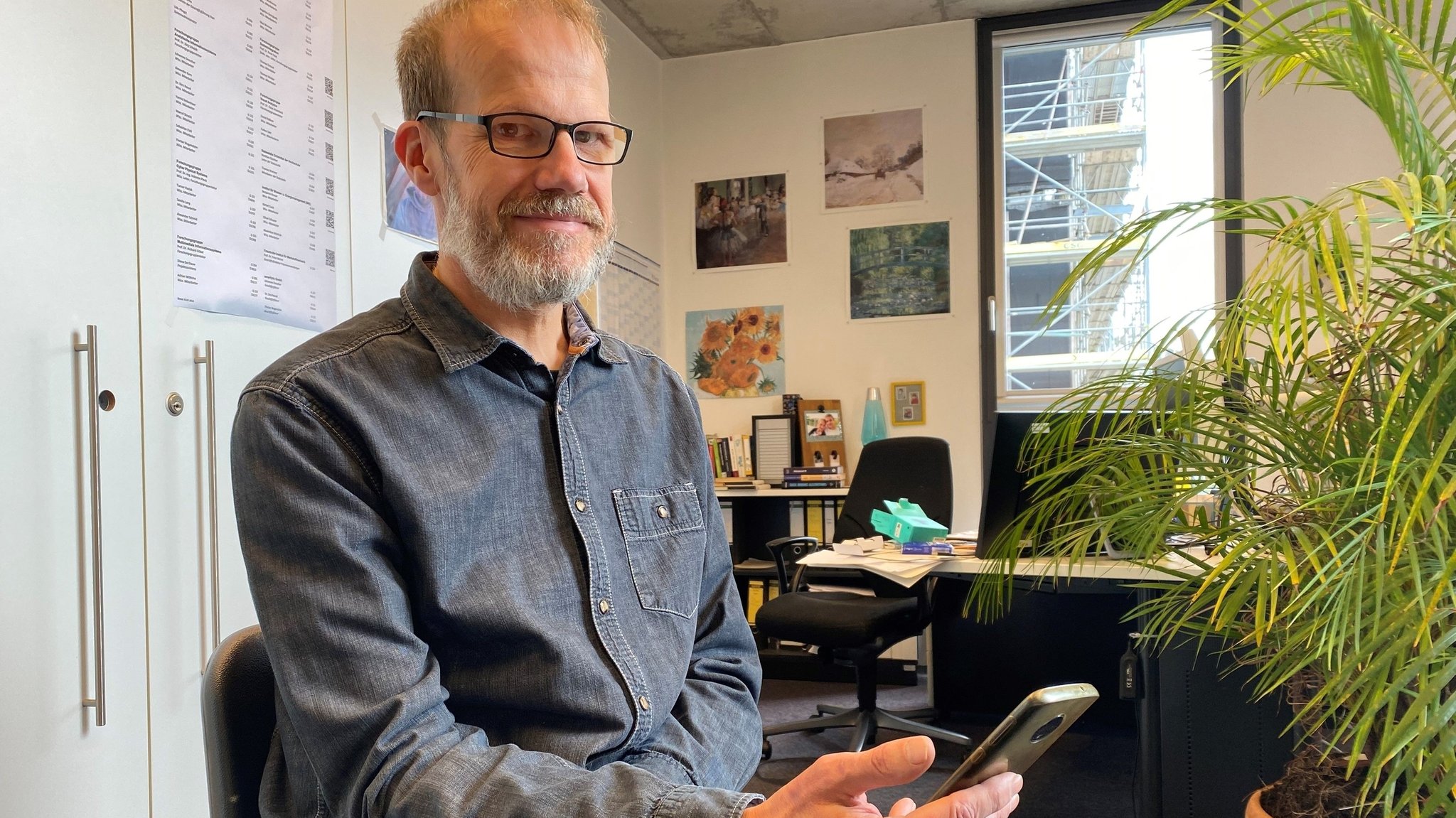 Professor Jörg Scheidt in seinem Büro mit Handy in der Hand.