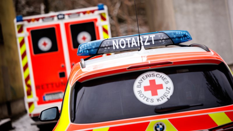 Symbolbild: Ein Notarzteinsatzfahrzeug steht während eines Rettungseinsatzes an einem Einsatzort geparkt hinter einem Rettungswagen vom Bayerischen Roten Kreuz.