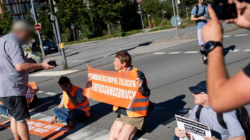 Klimaaktivisten der "Letzten Generation" bilden am 05.09.2023 in München eine Straßenblockade und werden von einem Autofahrer beschimpft.