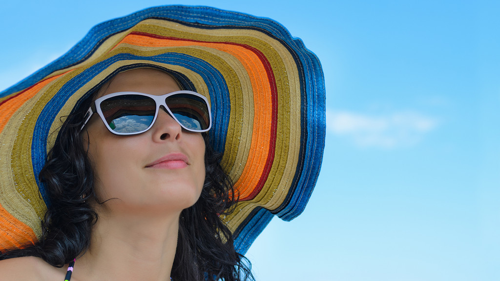 Frau mit Sonnenhut und Sonnenbrille vor blauem Himmel