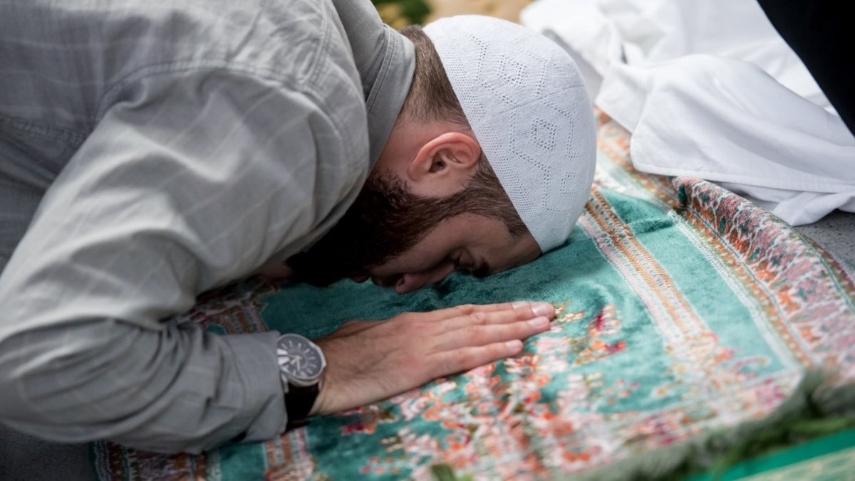 Ein Muslim nimmt in München an einem Freitagsgebet teil. Er kniet auf einem Gebetsteppich, den er mit Stirn und Händen berührt.