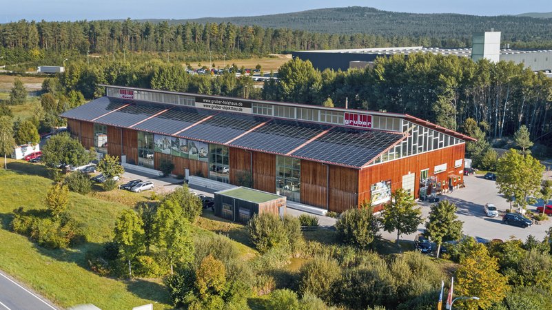 Eine Fabrikhalle mit Solarpaneelen umringt von Bäumen | Bild: Gruber Holzbau Eine Fabrikhalle mit Solarpaneelen umringt von Bäumen
