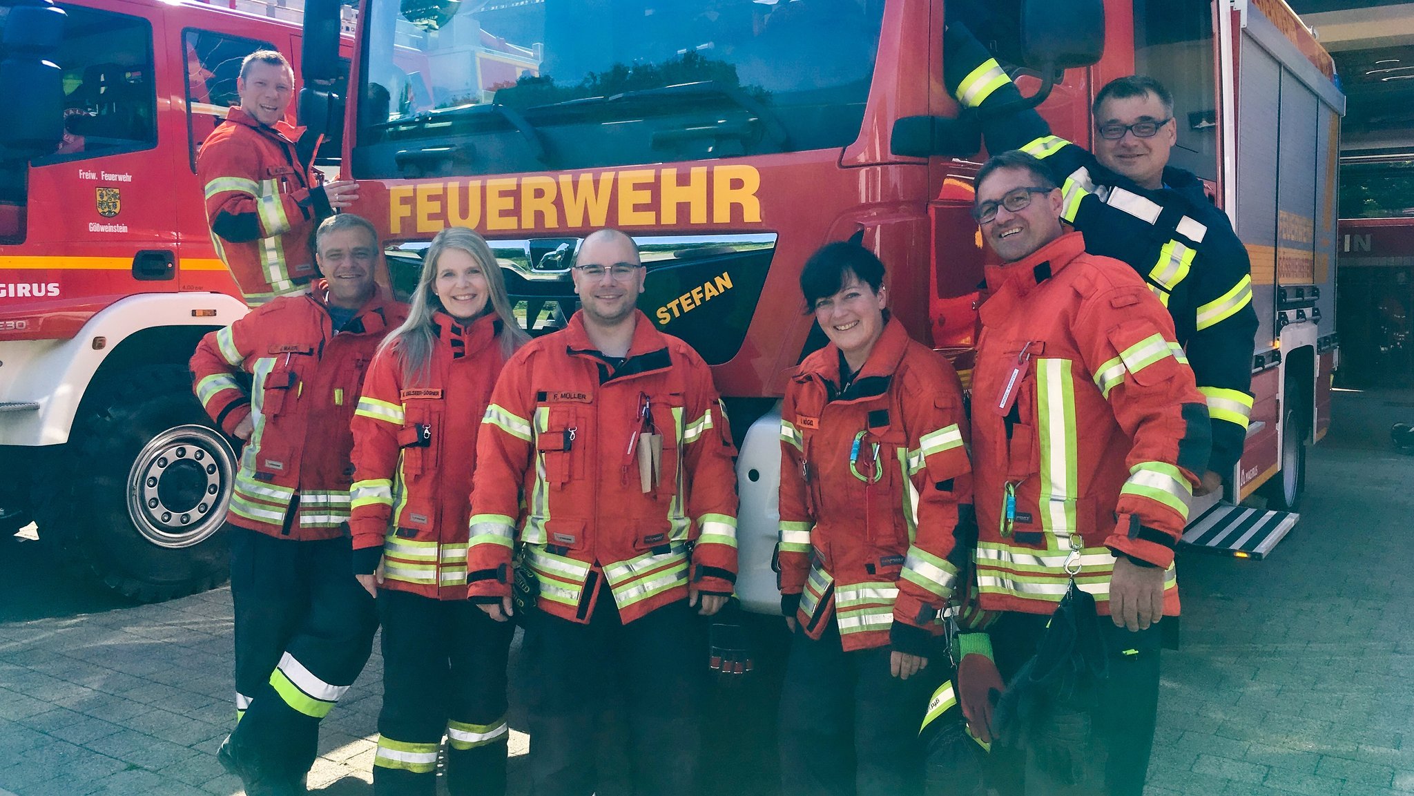 Männer und Frauen der Feuerwehr stehen vor ihrem Einsatzfahrzeug.