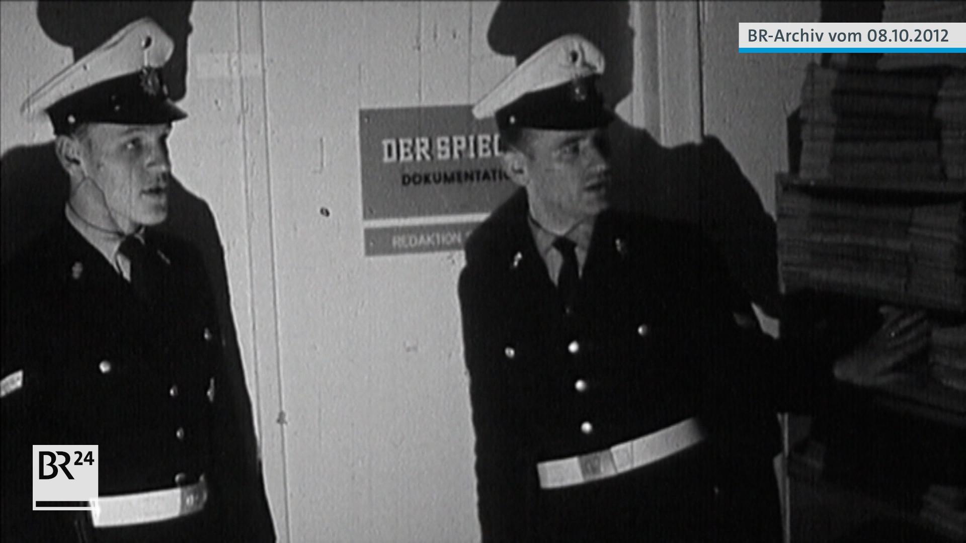 Zwei Polizisten stehen vor einer Tür mit einem Schild mit der Aufschrift  "Der Spiegel" Dokumentation