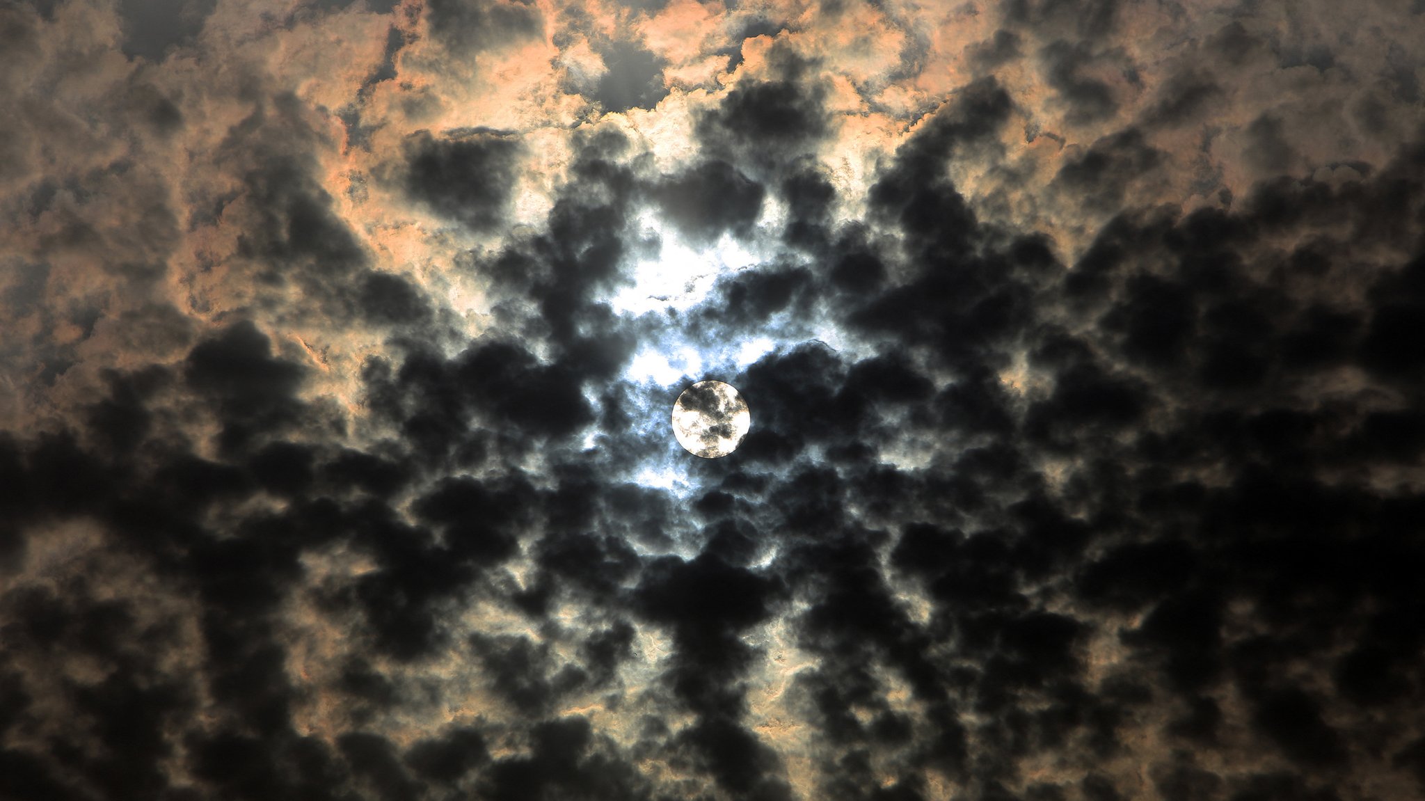 Die Sonne scheint durch sehr dunkle Wolken hindurch