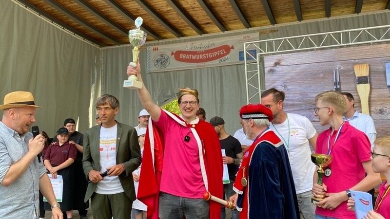 Der Bratwurstkönig Dirk Freyberger hält seinen Pokal bei der Preisverleihung in die Höhe.
