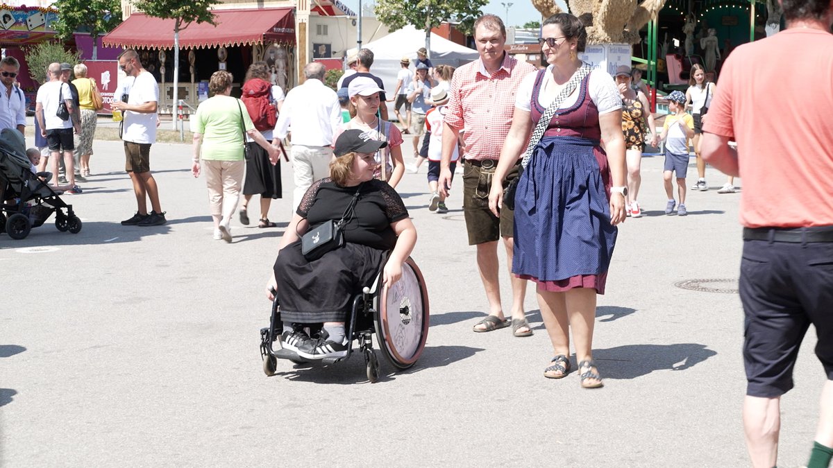 Eine Familie mit zwei Erwachsenen und zwei Kindern auf dem Gäubodenvolksfest in Straubing. Ein Kind sitzt im Rollstuhl. Die ganze Familie hat traditionelle Tracht an.