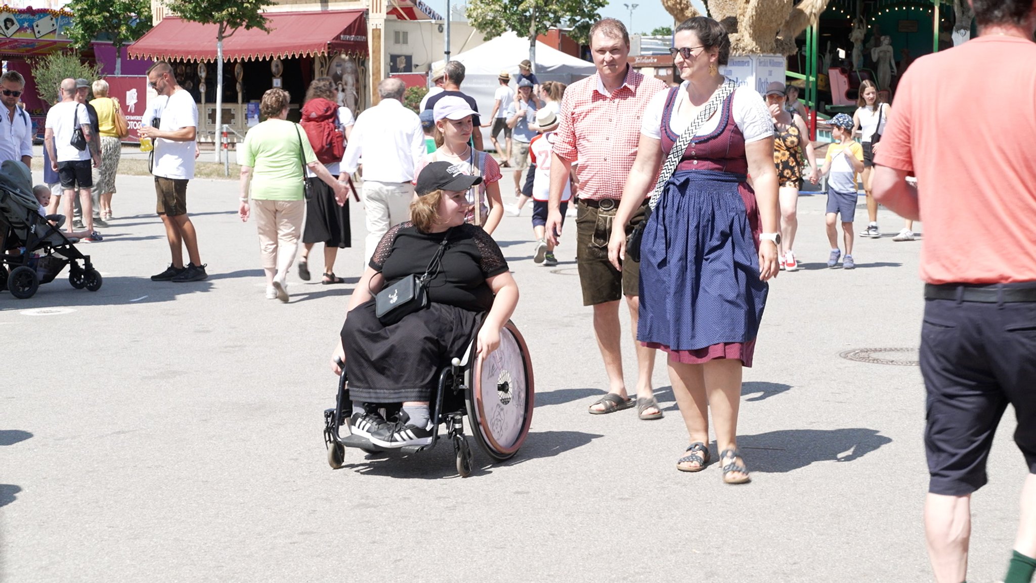 Eine Familie mit zwei Erwachsenen und zwei Kindern auf dem Gäubodenvolksfest in Straubing. Ein Kind sitzt im Rollstuhl. Die ganze Familie hat traditionelle Tracht an.