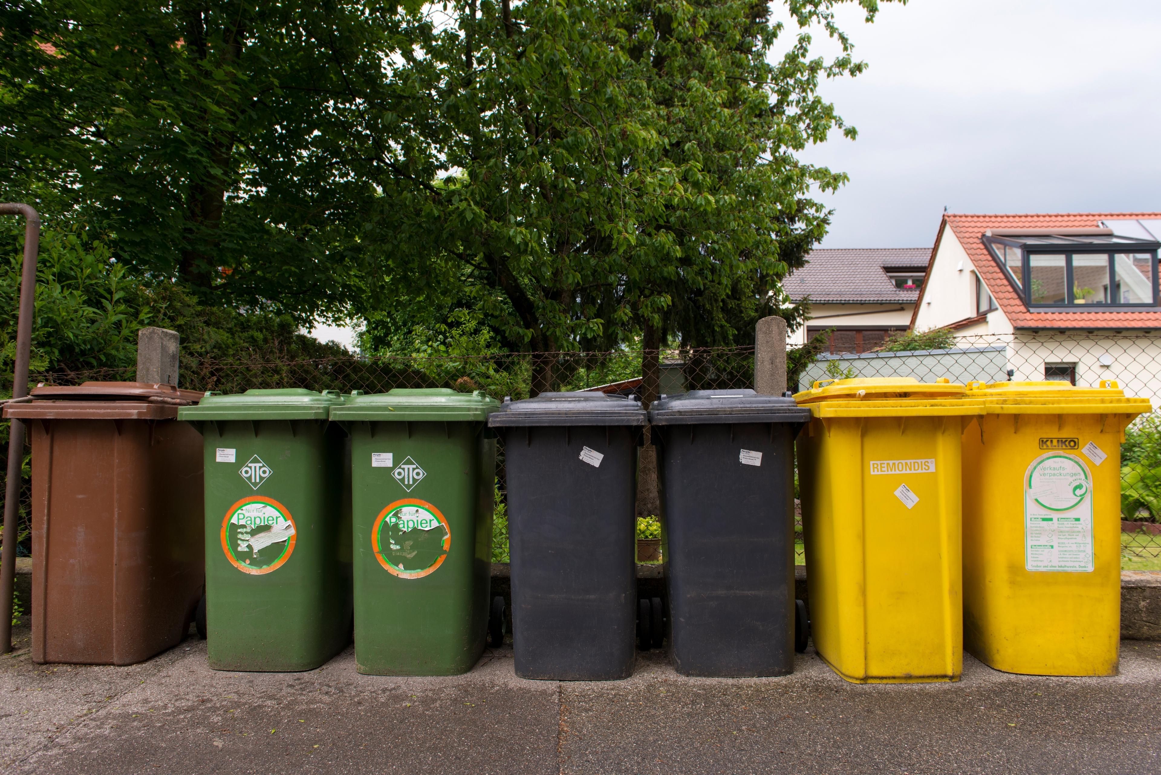 (Symbolbild) Mehrere Mülltonnen für Kompost, Papier, Restmüll und Verrkaufsverpackungen stehen nebeneinander an einem Zaun in Augsburg