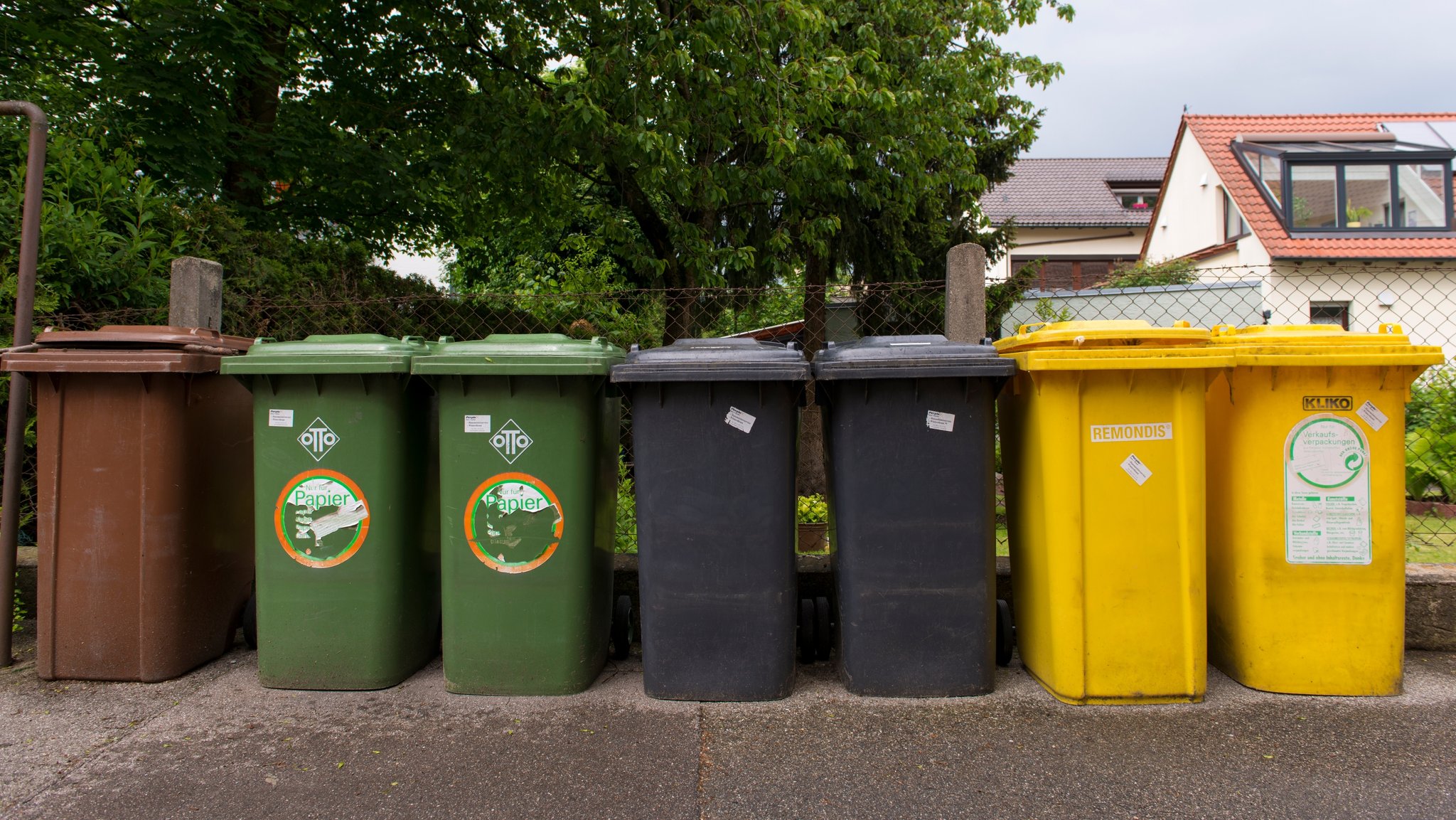 (Symbolbild) Mehrere Mülltonnen für Kompost, Papier, Restmüll und Verrkaufsverpackungen stehen nebeneinander an einem Zaun in Augsburg