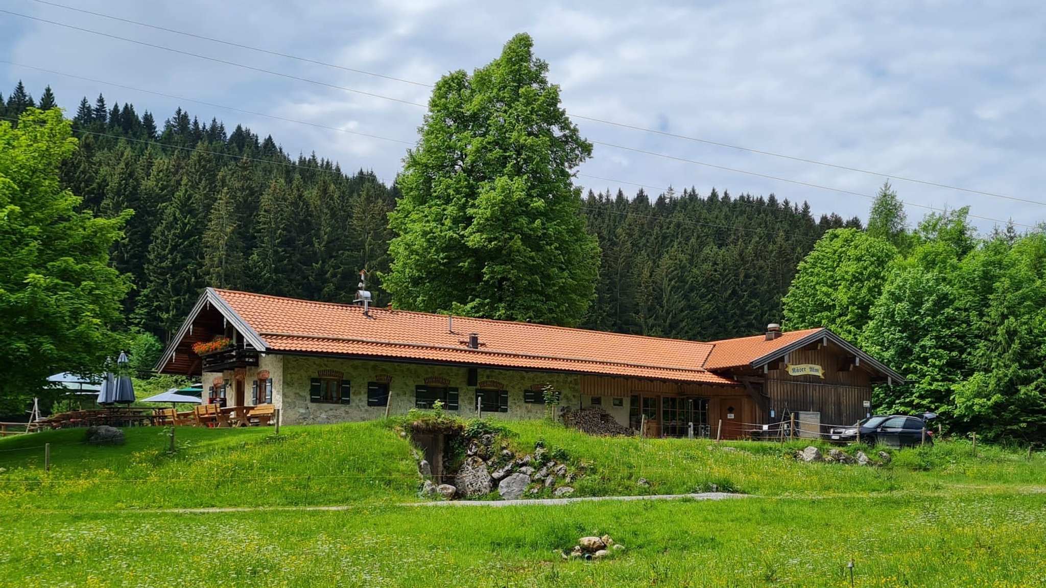 aus Stein gebaute Alm mit Terrasse, im Vordergrund saftig grüne Wiesen -die Käseralm am Samerbergseralm leicht zu erreichen