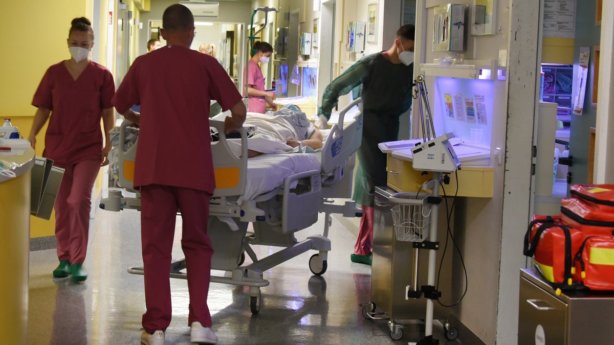 Pfleger schieben einen Patienten in einem Bett über den Flur der Intensivstation