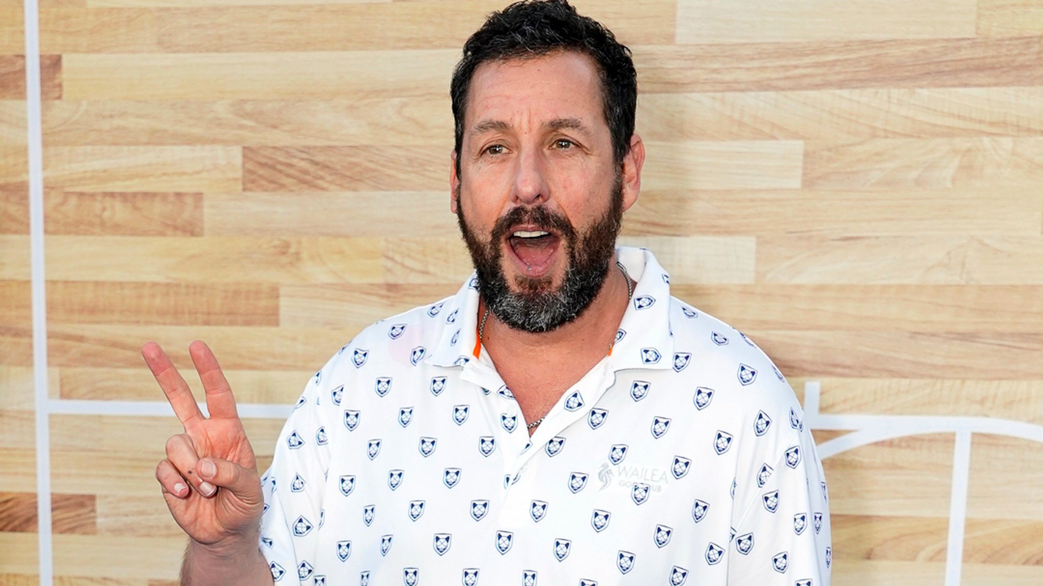 Man sieht Adam Sandler im weißen Hand und mit der rechten Hand, die das Victory-Zeichen macht, bei der Premiere des Netflix-Films "Hustle" 2022 im Regency Village Theatre in Los Angeles herumalbern. 