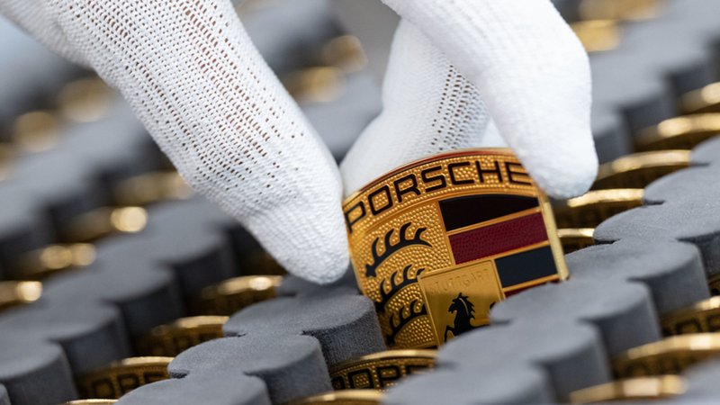 Ein Mitarbeiter der Porsche AG zeigt in einer Produktionshalle des Porsche-Stammwerks das Porsche-Logo. | Bild: dpa-Bildfunk/Marijan Murat Ein Mitarbeiter der Porsche AG zeigt in einer Produktionshalle des Porsche-Stammwerks das Porsche-Logo.