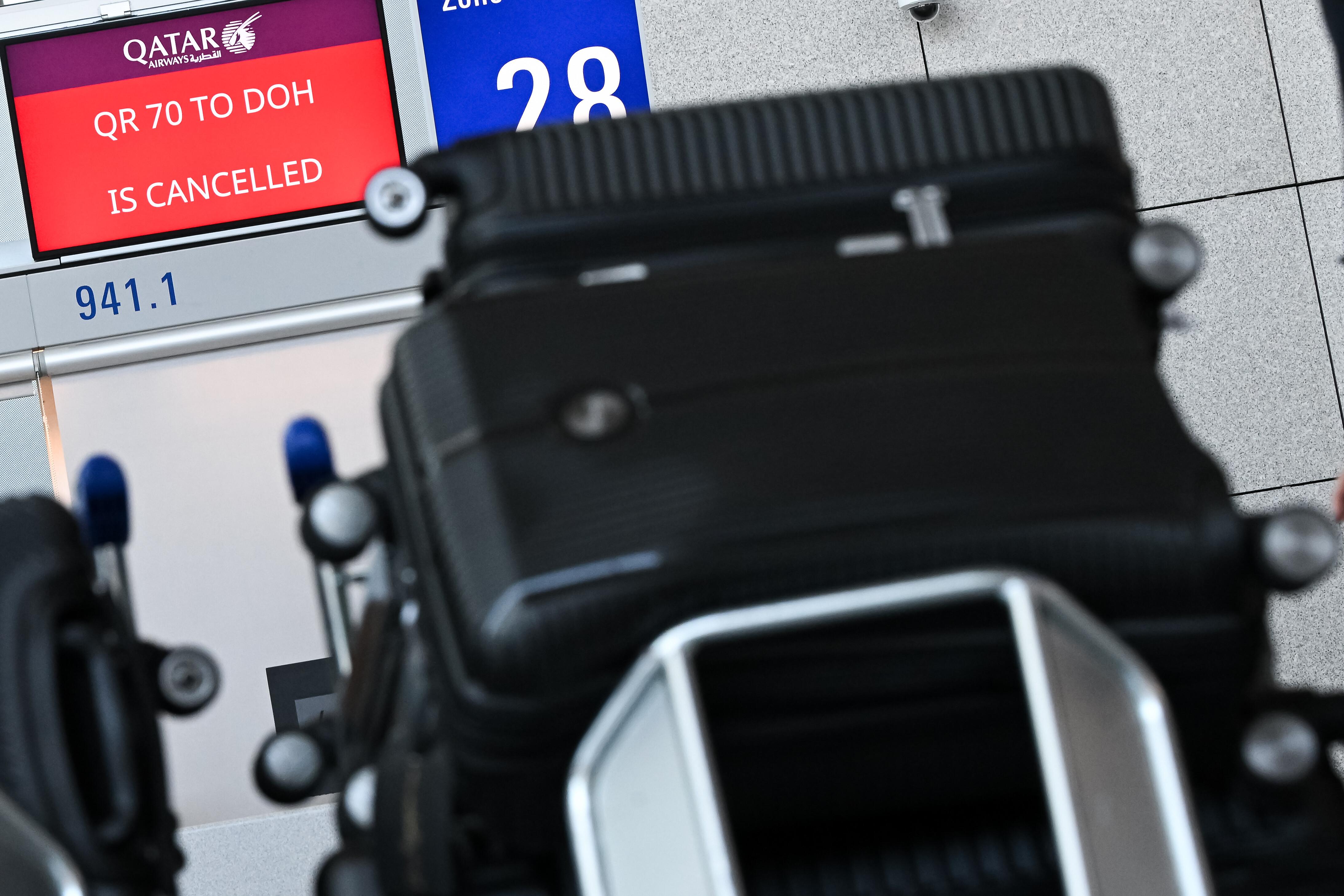 Koffer von Reisenden vor einem Bildschirm, auf dem ein annullierter Flug von Qatar Airways angezeigt wird.