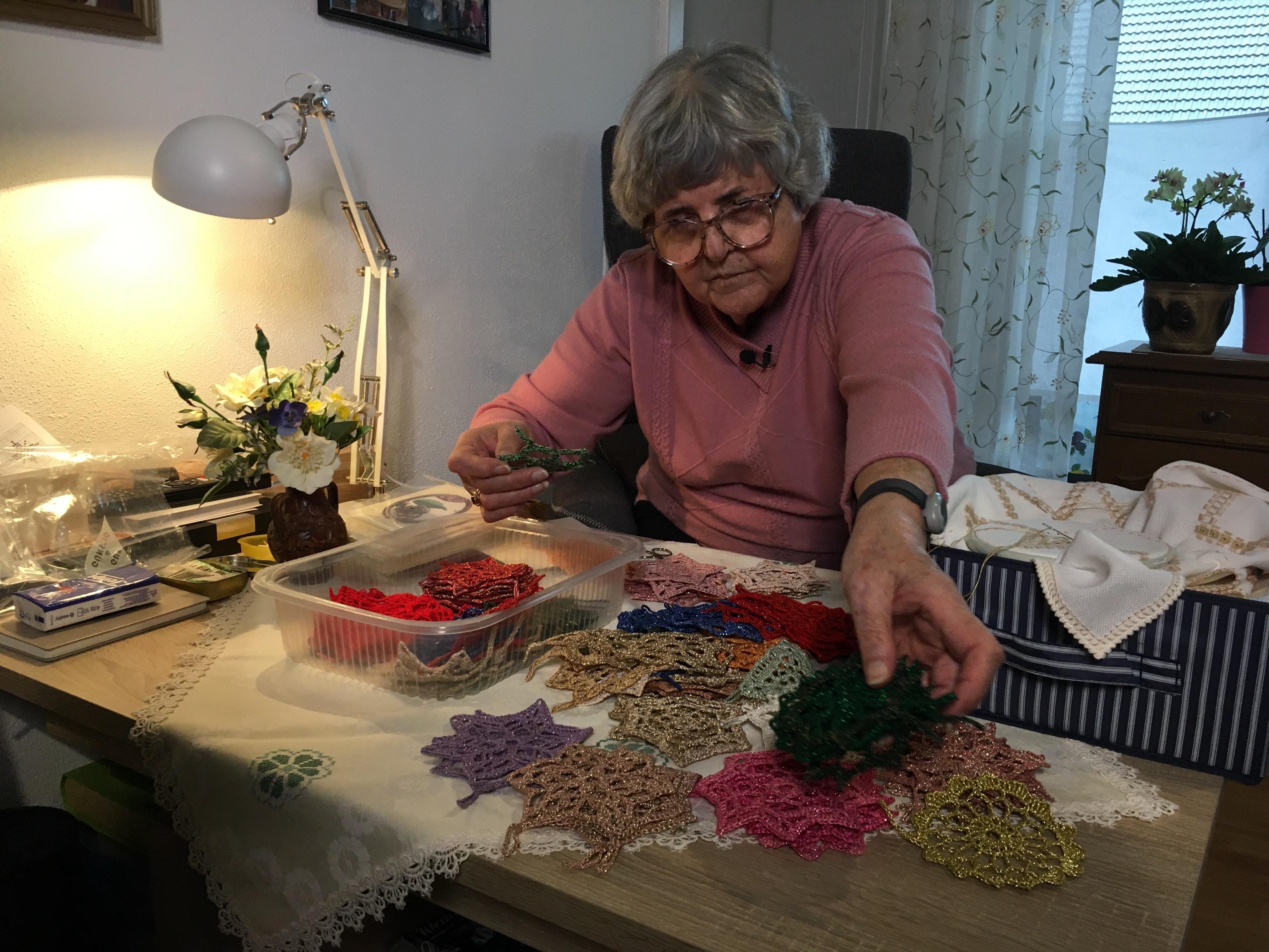 Anni Kohlmann sitzt an einem Tisch, vor ihr liegen unzählige gehäkelte, bunte Sterne. 