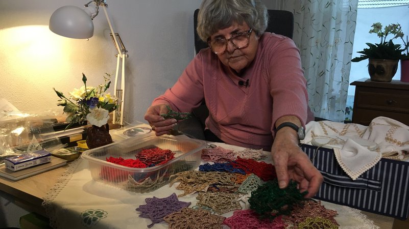 Anni Kohlmann sitzt an einem Tisch, vor ihr liegen unzählige gehäkelte, bunte Sterne. | Bild: BR/Tobias Burkert Anni Kohlmann sitzt an einem Tisch, vor ihr liegen unzählige gehäkelte, bunte Sterne.