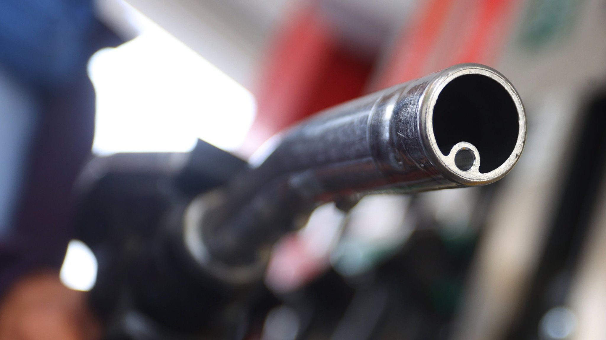 Eine Frau hält an einer Tankstelle vor einer Zapfsäule eine Zapfpistole. 