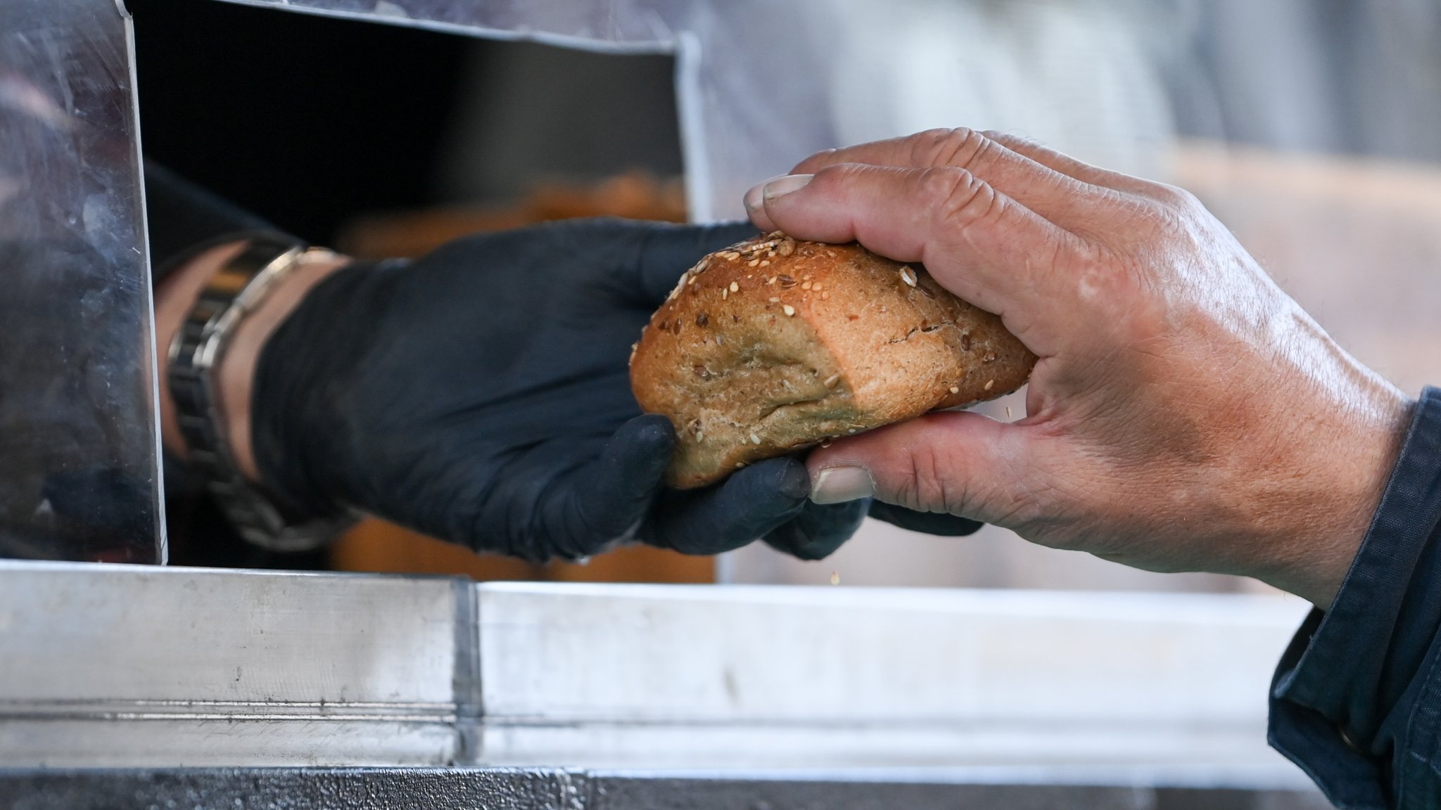 Ein Mann reicht durch ein Loch in einer Plexiglasscheibe ein Brötchen weiter.