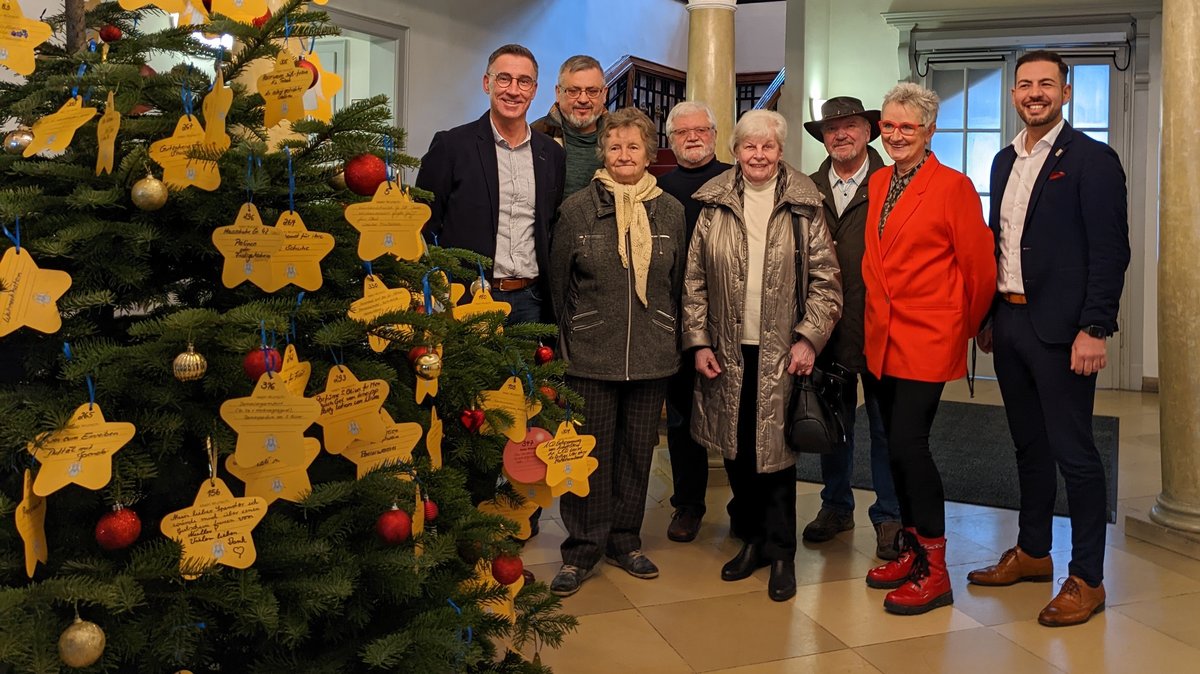 Ein Weihnachtsbaum mit gelben Wünschesternen, daneben mehrere Mitglieder des Seniorenbeirats.