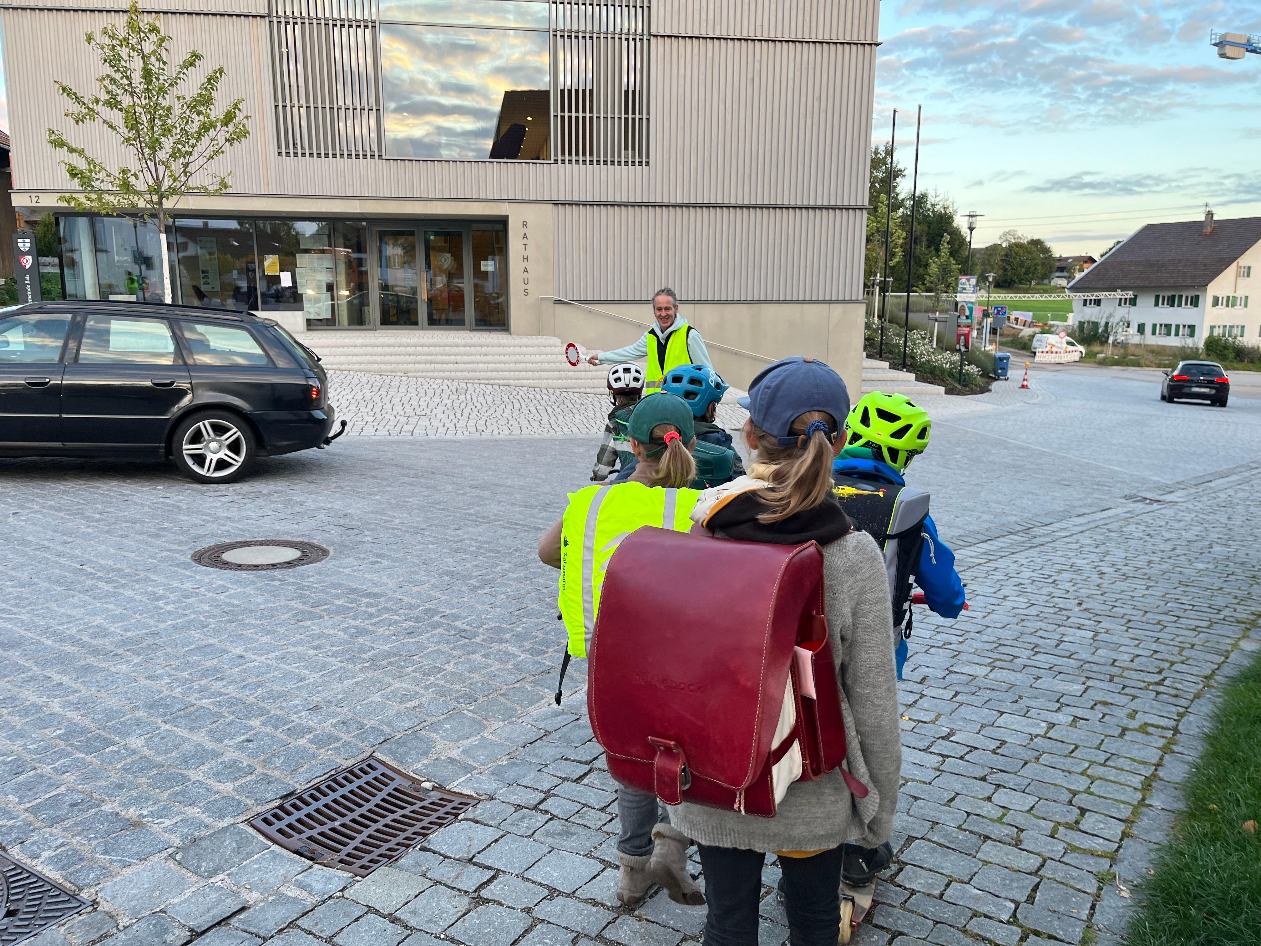 Kinder werden von einem Schulweghelfer über die Straße geleitet.
