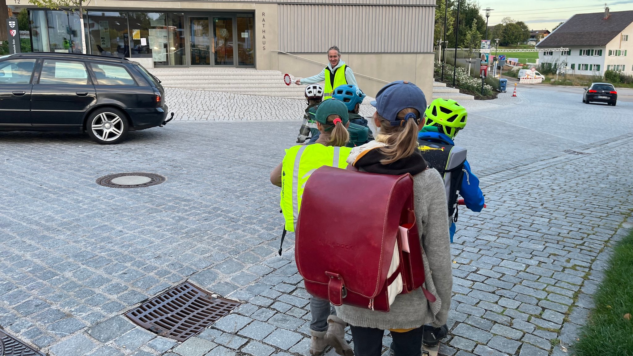 Kinder werden von einem Schulweghelfer über die Straße geleitet.