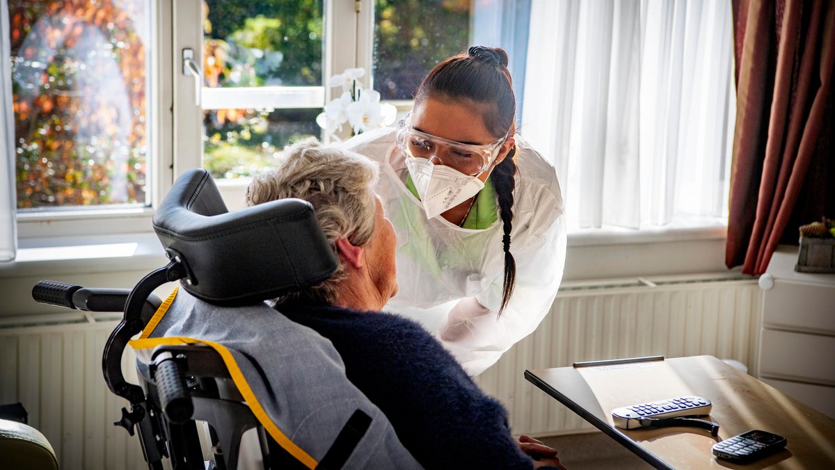 Eine Pflegerin spricht mit einer älteren Frau in einem Rollstuhl.