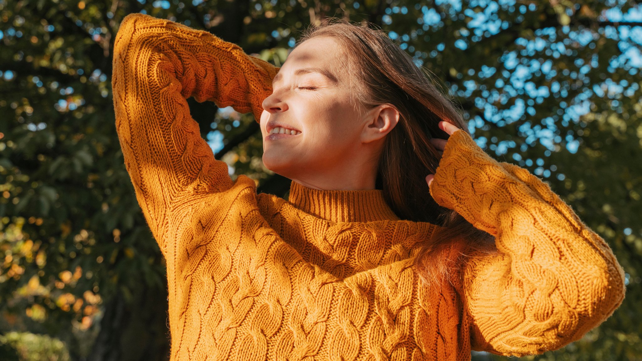 Eine Frau im orangen Pullover schaut genießerisch in die Herbstsonne