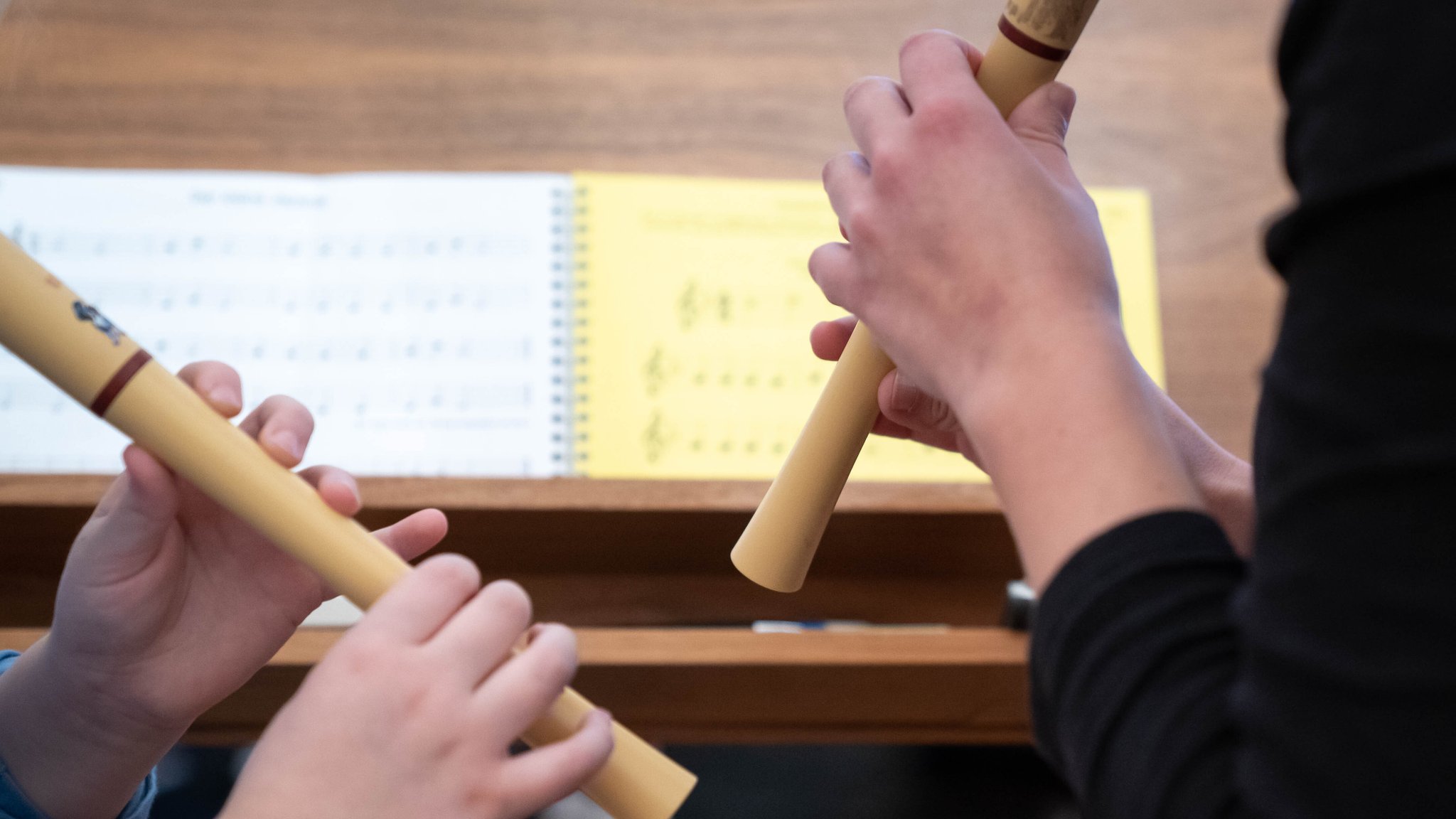 Hände eines Kindes, das eine Blockflöte hält, daneben Lehrerin mit Blockflöte